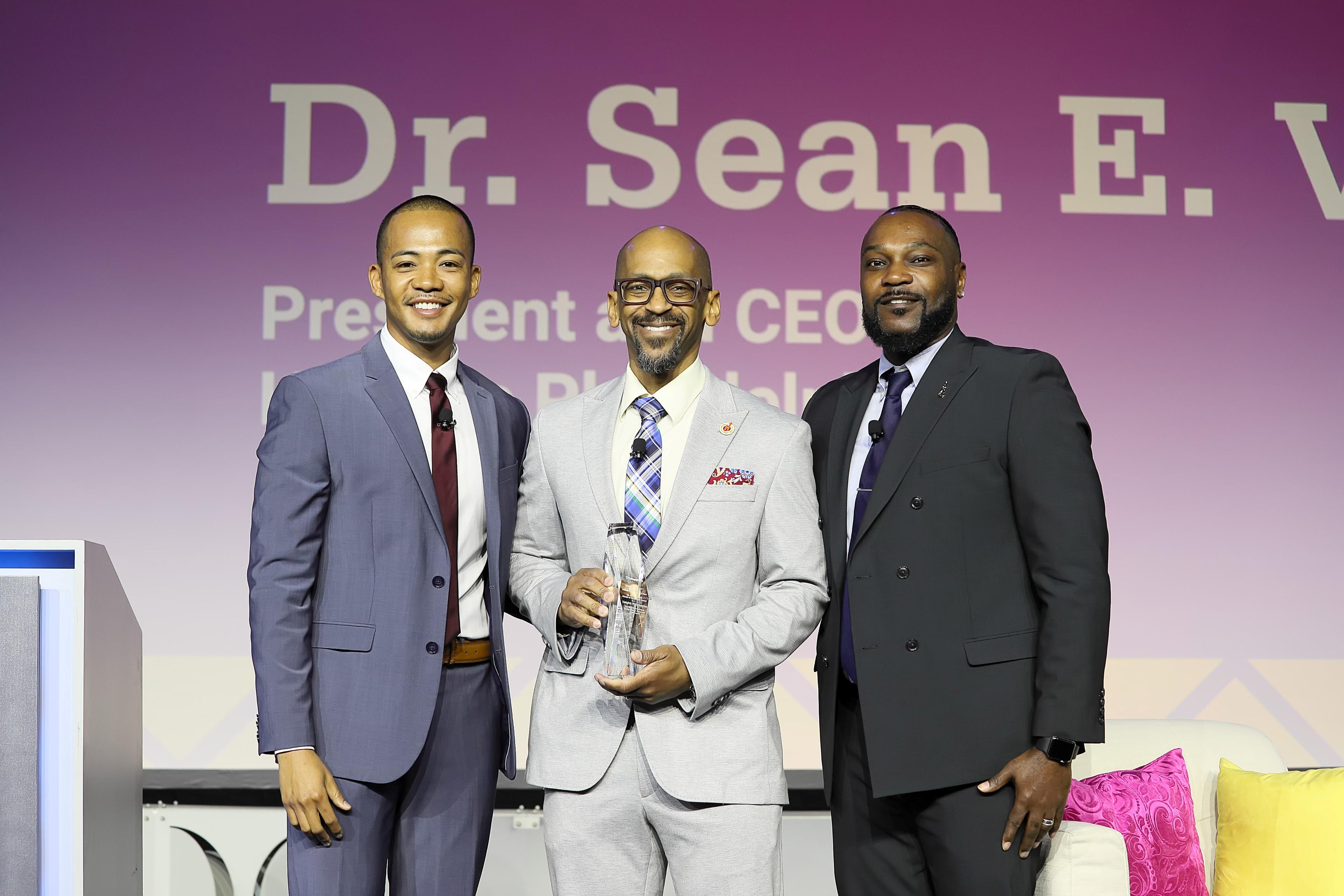 Three speakers pose for a photo on the main stage with an award.